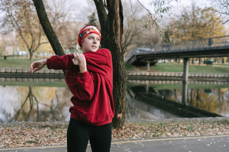 a girl in a red sweater stands in front of a pond