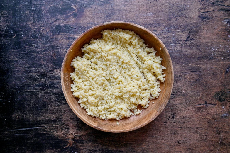 a wooden bowl filled with rice sits on top of a wood table