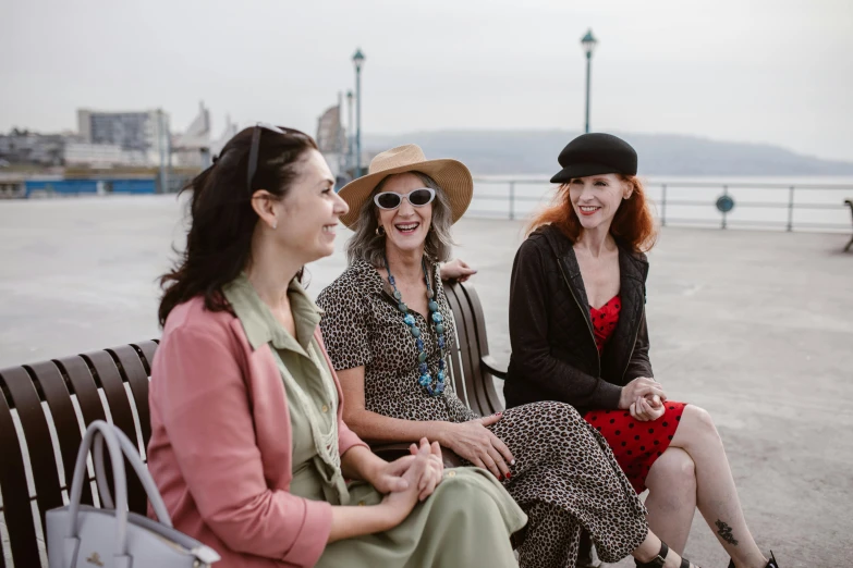 three women are talking on a bench by the water