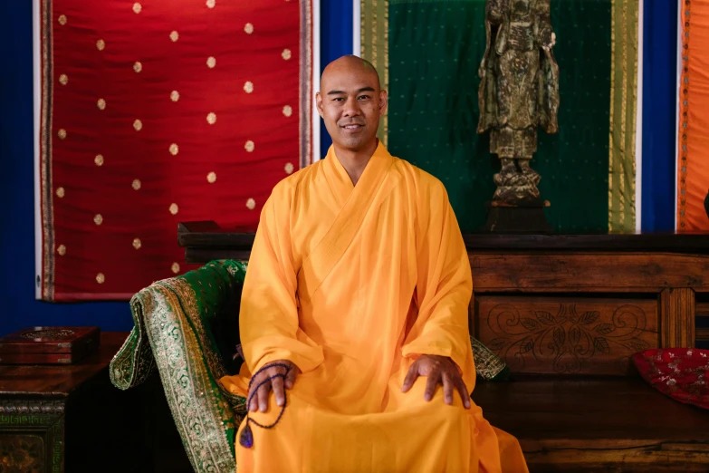 a man in orange robes sitting next to a rug