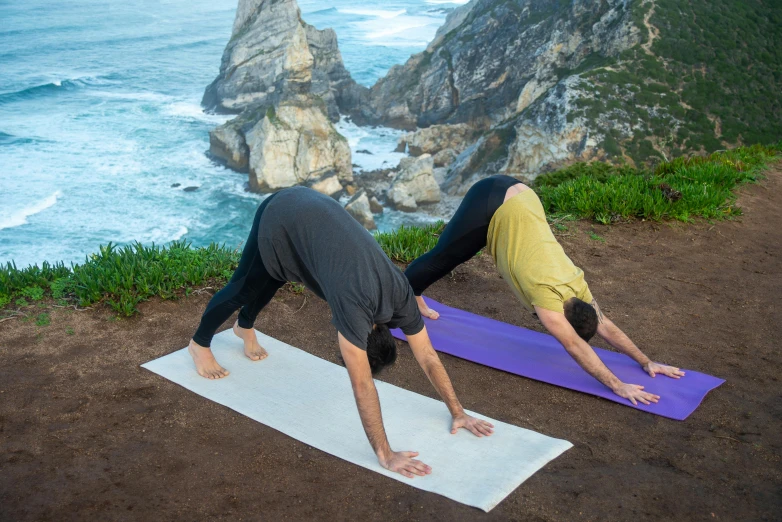 two men doing yoga in front of the ocean