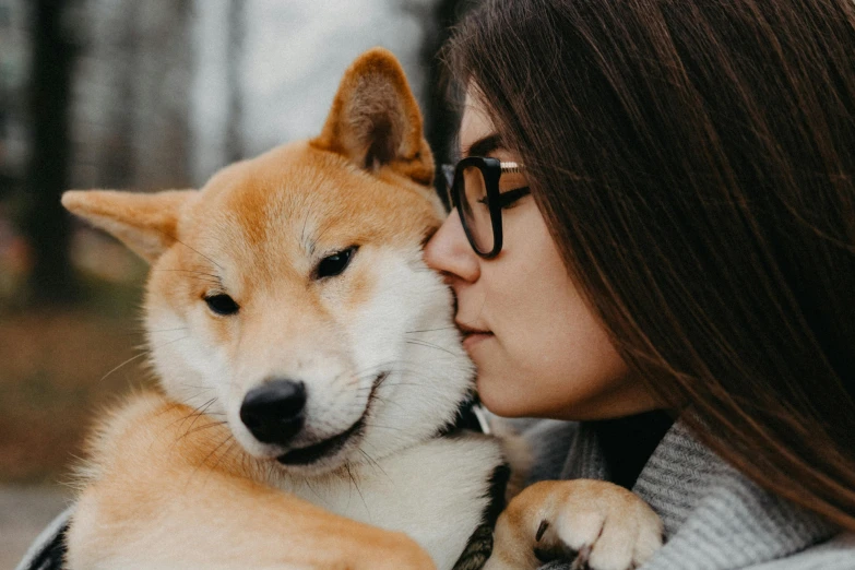 a woman kissing her dog on the head with its face close to her chest