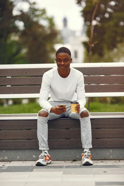 a man sitting on a bench in front of a railing holding a cup