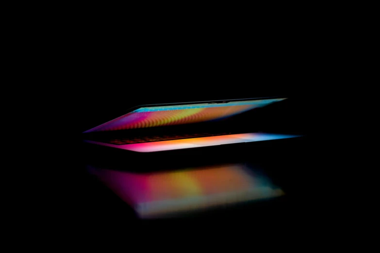 an apple laptop in dark room with rainbow reflected on surface