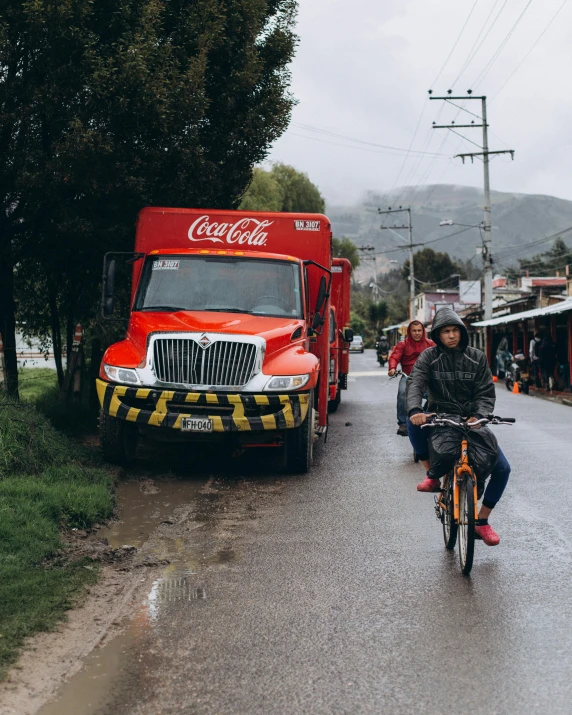 people riding bikes on the side of the road with trucks behind them