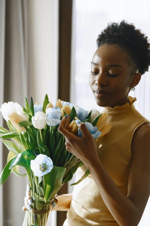 a woman holds flowers on a vase in front of a window