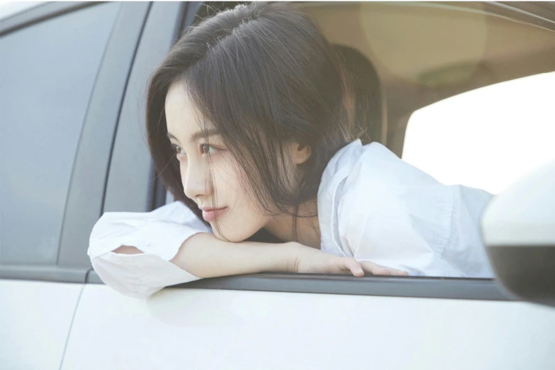 an asian woman sitting in a white car, holding her head out the window
