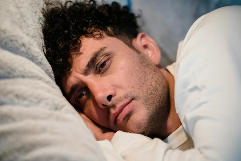man laying with eyes closed in bed staring at camera
