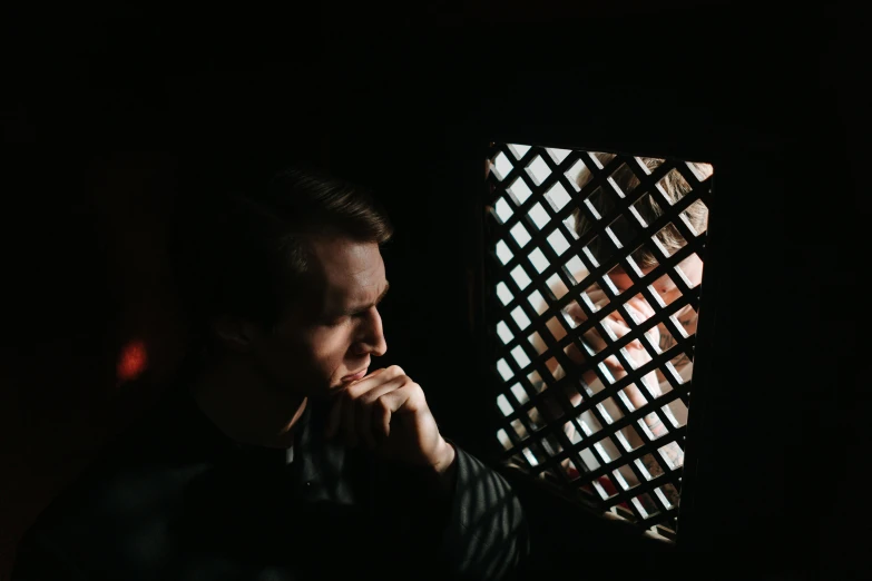 a man in dark lighting standing and touching his chin