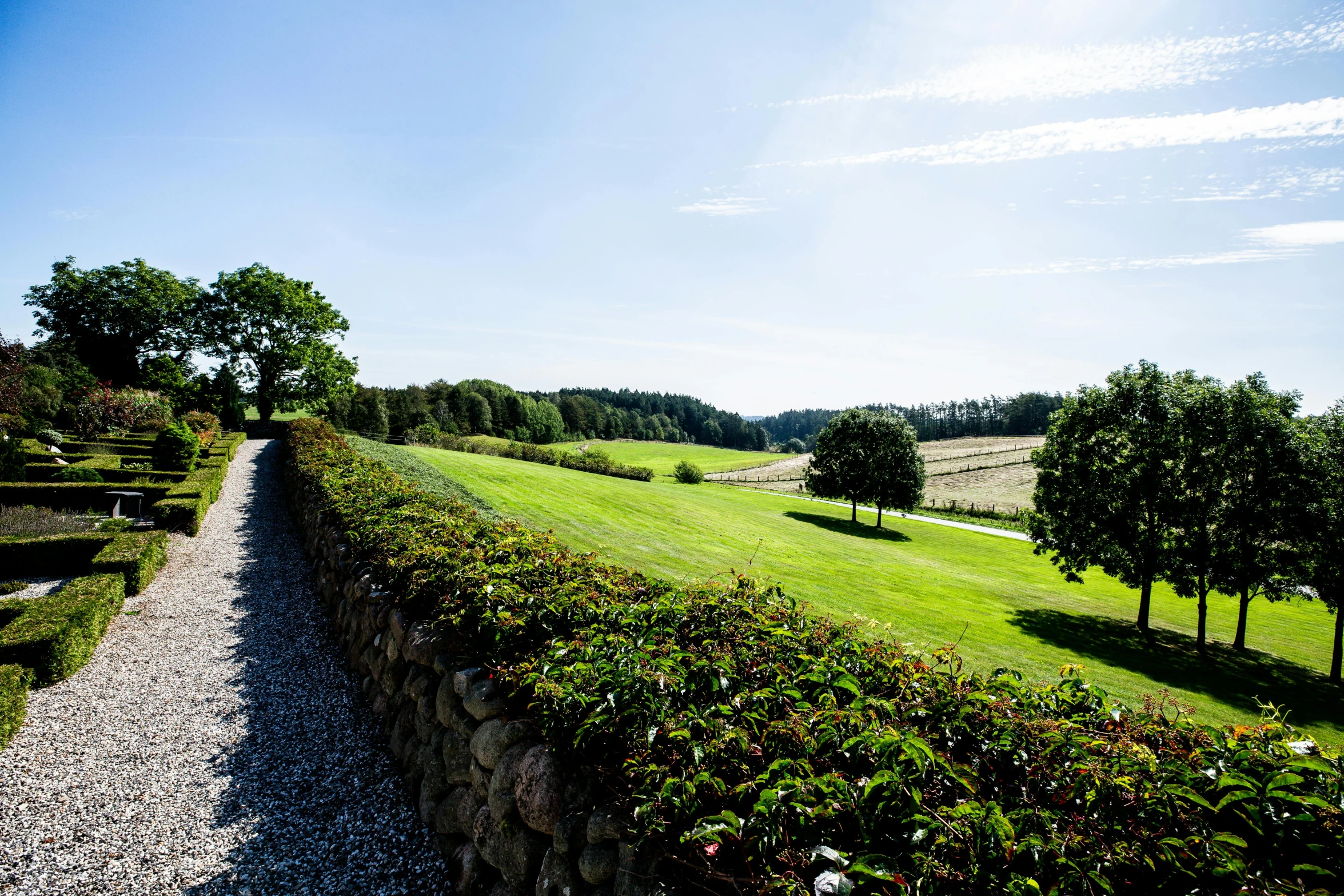 a stone wall with a field, trees and flowers on top