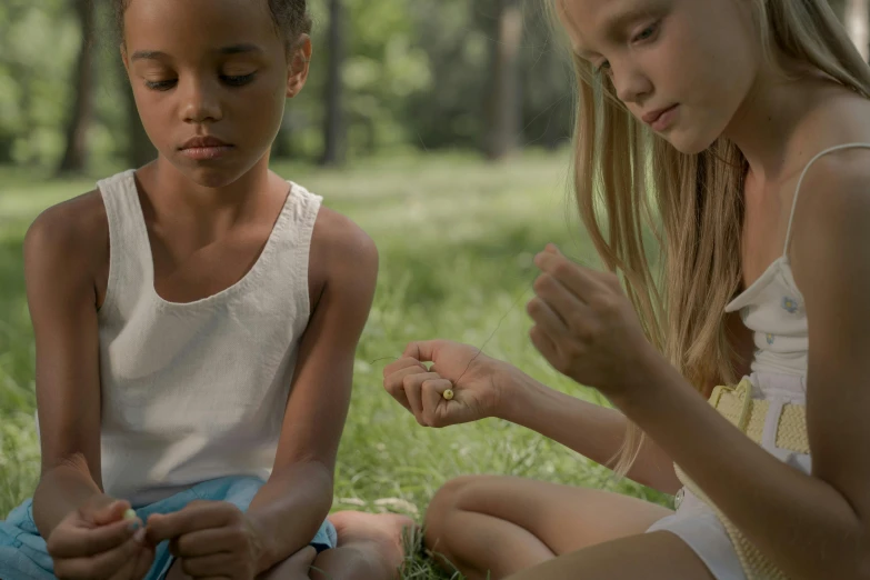 two children are sitting on the grass playing with their cellphones