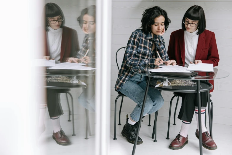 two girls writing on paper in the reflection of another girl