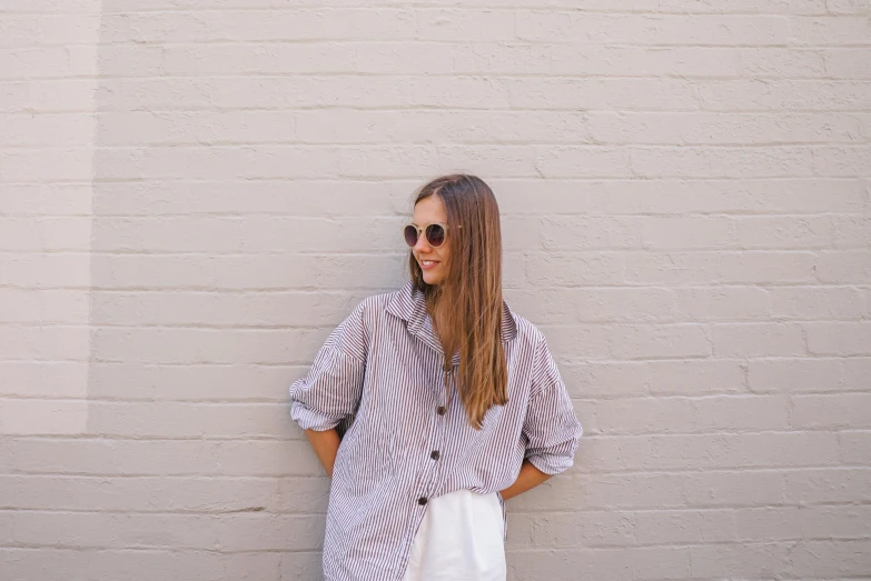 a young woman stands in front of a brick wall