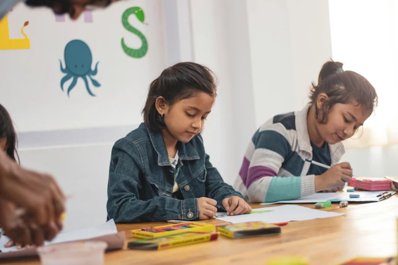 two girls are sitting at a table writing and doing crafts