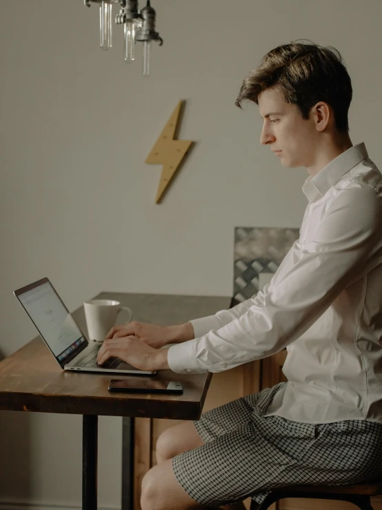 the man is sitting with a coffee mug using his laptop