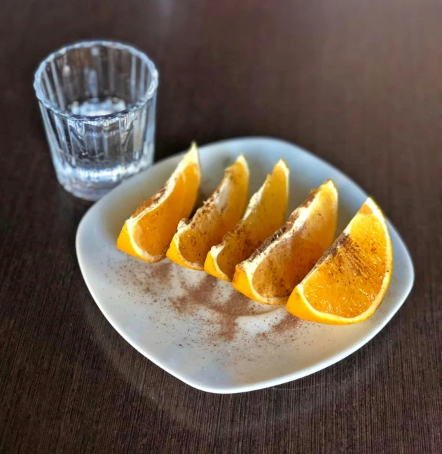 a plate of cut oranges on a table next to a glass