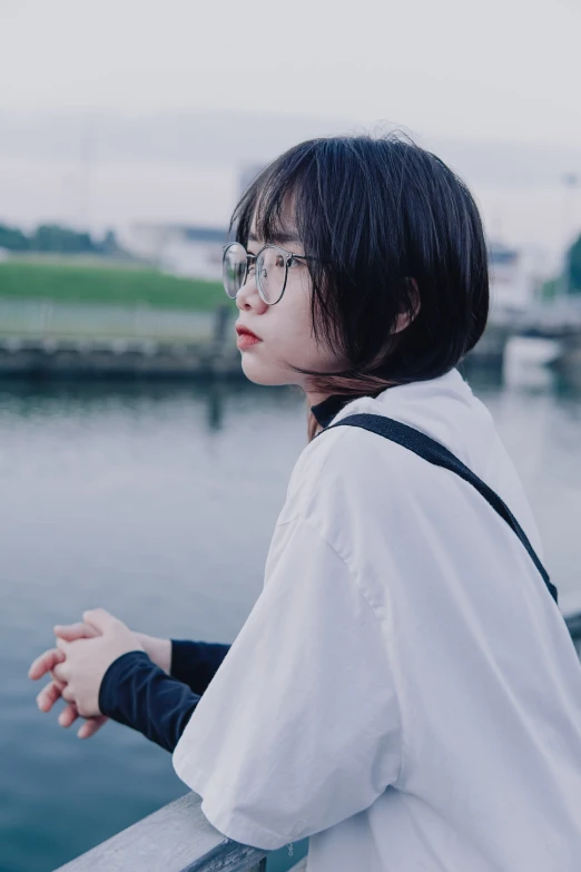 a person with glasses, leaning on a rail near water