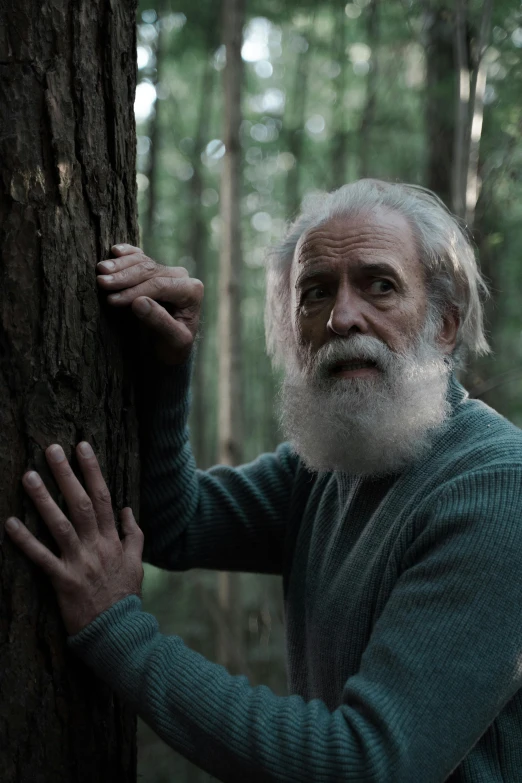 an older man holding onto a tree in the woods