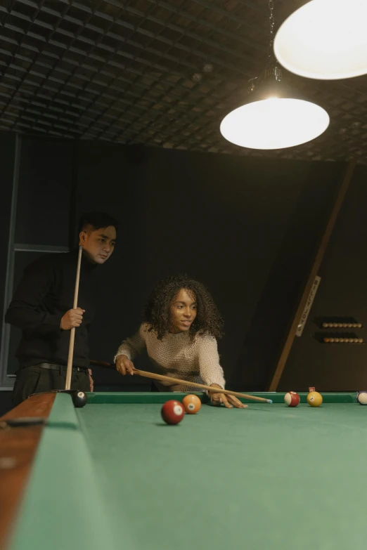 a girl is holding a cue, while a guy in the background plays pool