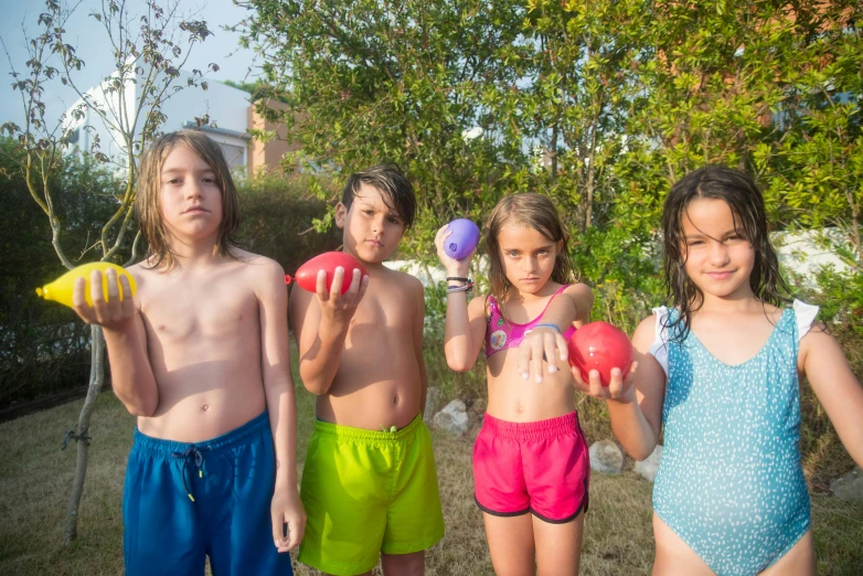 several children holding balls in their hands standing in front of a green bush