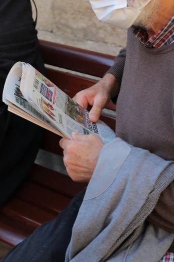 a man wearing a face mask reads the news paper