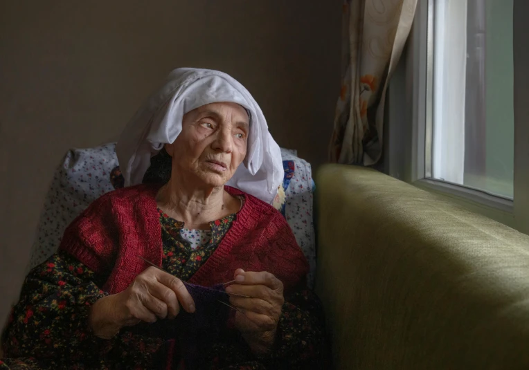 an older woman sitting on a couch with a white bandanna
