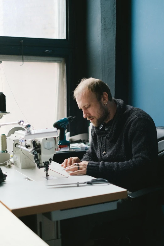 the man is working on soing while using a sewing machine