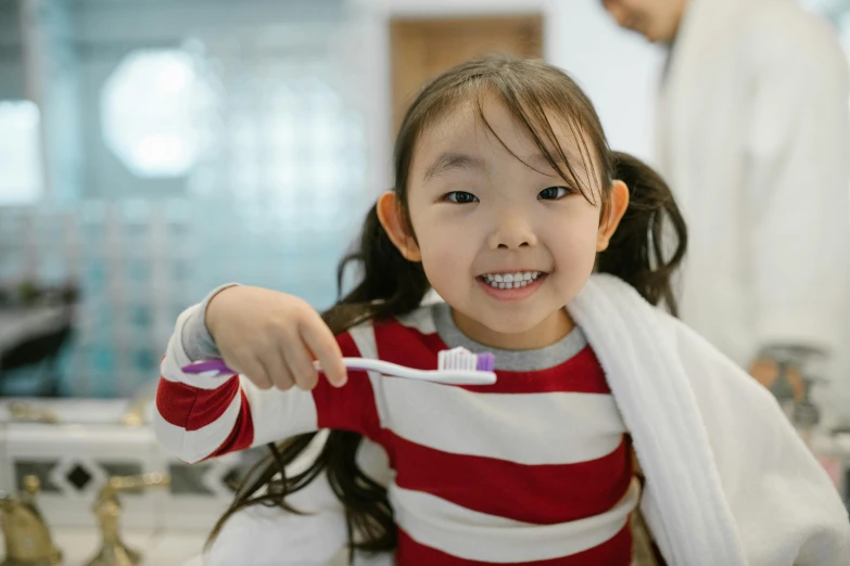 a little girl brushing her teeth and wearing a red and white  shirt