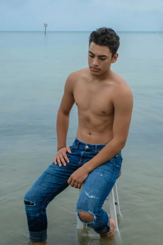shirtless man sitting in the water and looking at soing