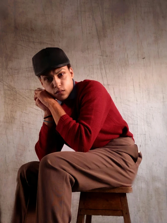 young man sitting on stool in hat and red shirt