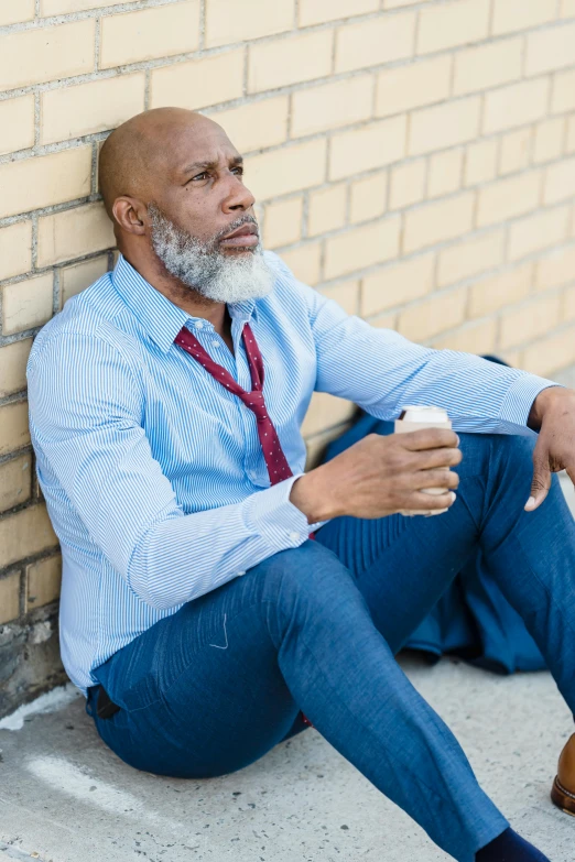 a man sitting against a brick wall holding a cup