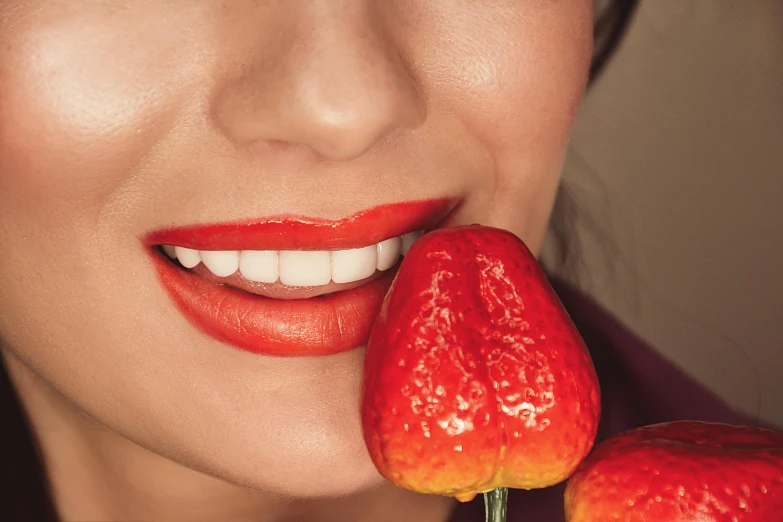 a person with orange lipstick on holding up a red fruit