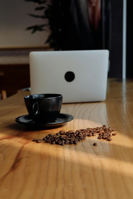 coffee beans spilled from a cup next to a white laptop computer