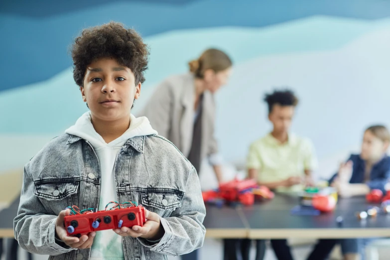 a boy stands in front of an art exhibit holding toy cars