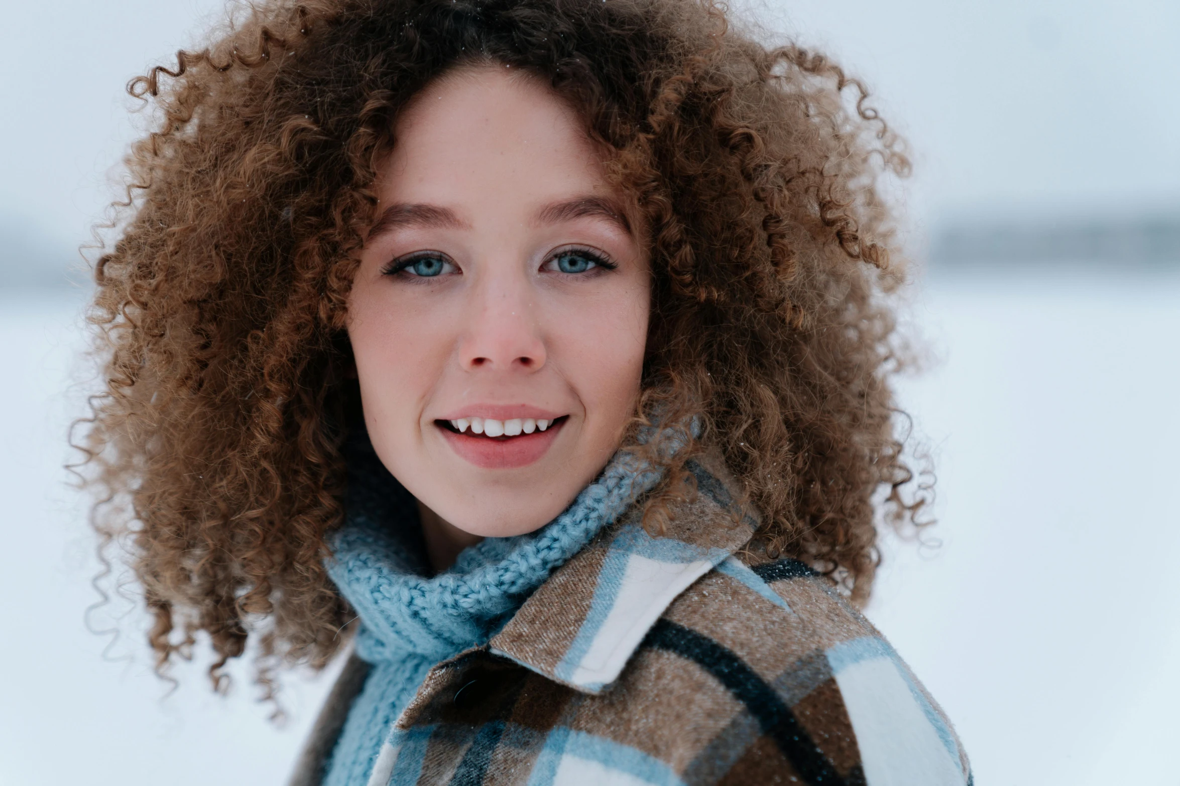 a woman with curly hair smiles in front of snow