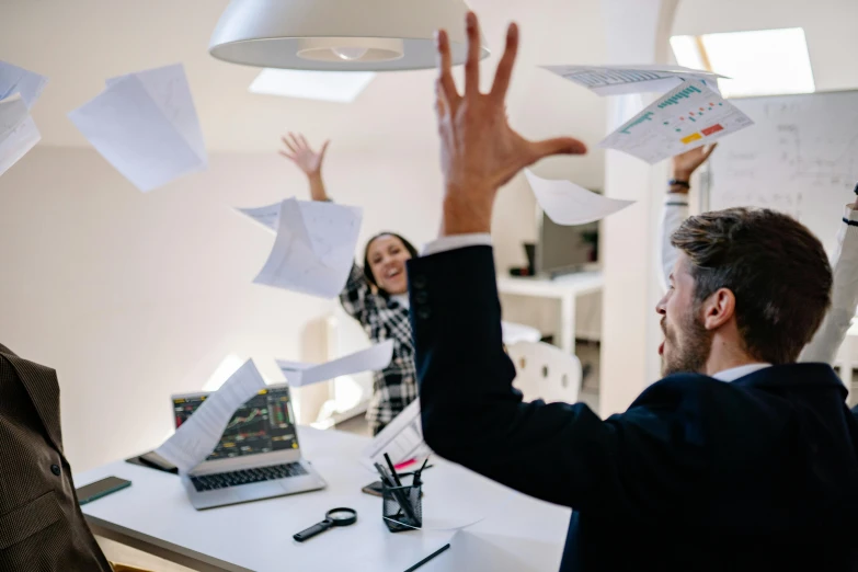 two men are sitting at a desk and throwing papers