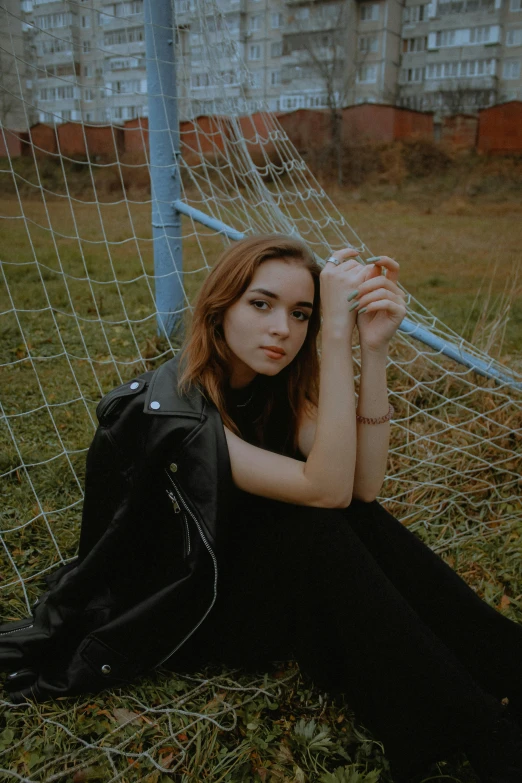 a beautiful young woman in black sitting on grass next to a soccer goal