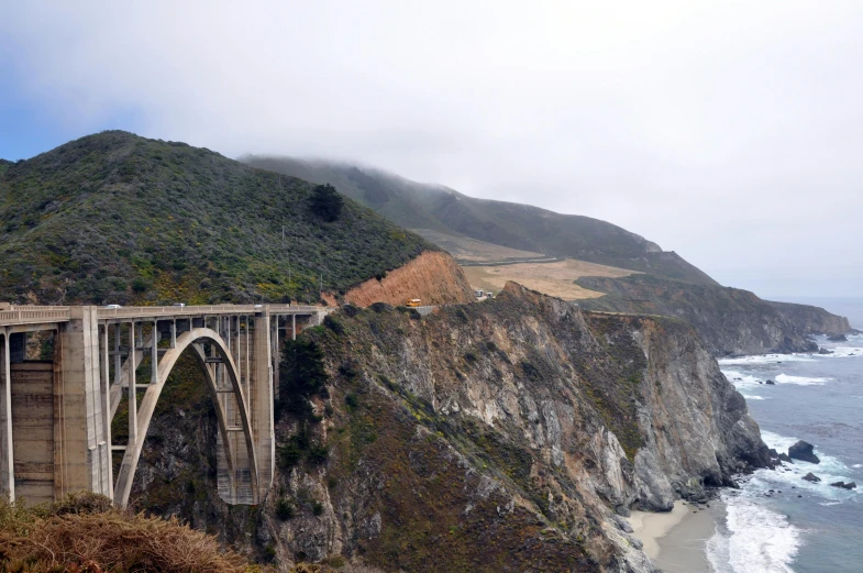 a bridge spanning the ocean and mountains on a cloudy day