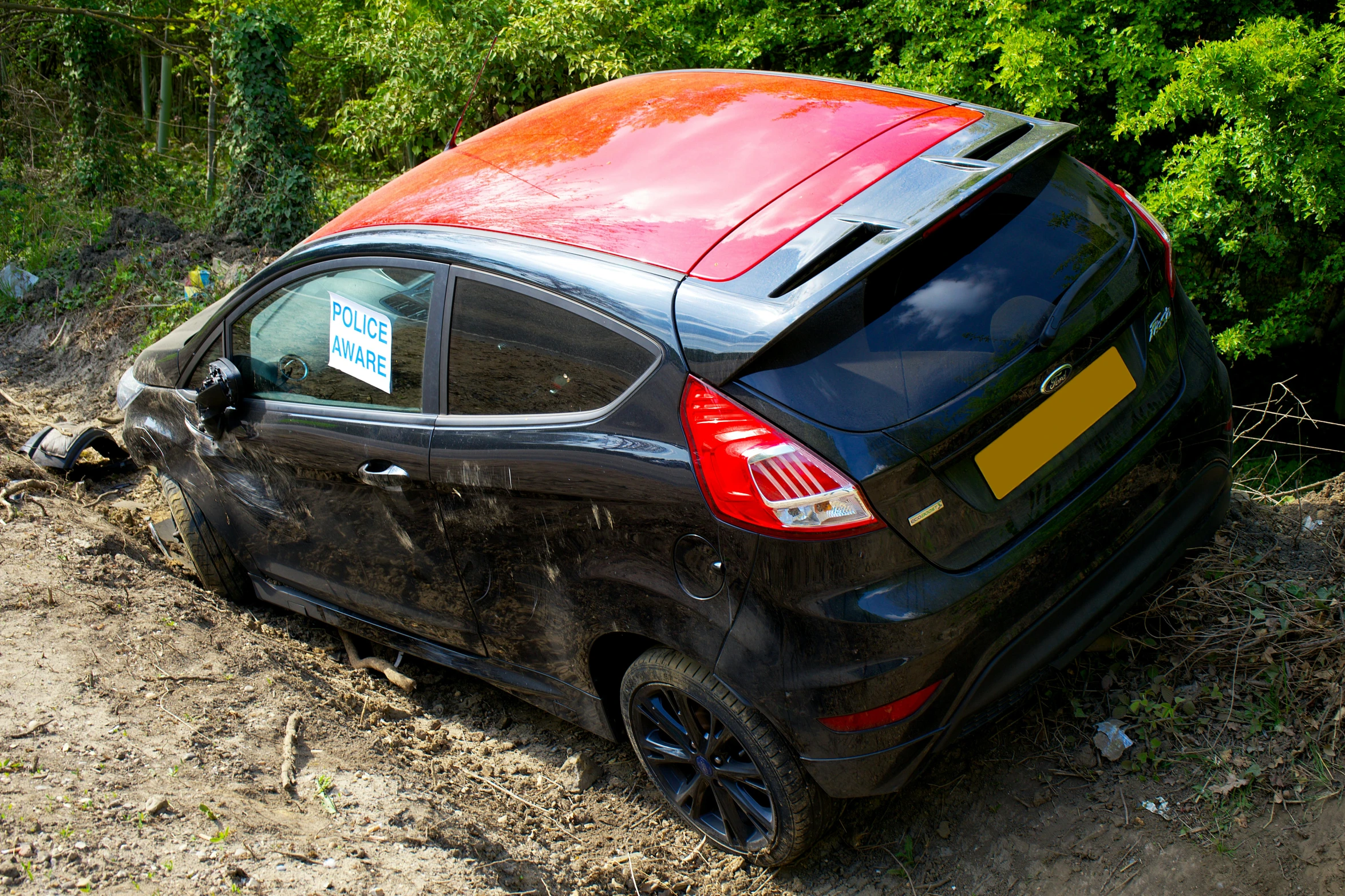 a small black car with red stripes parked on a muddy road