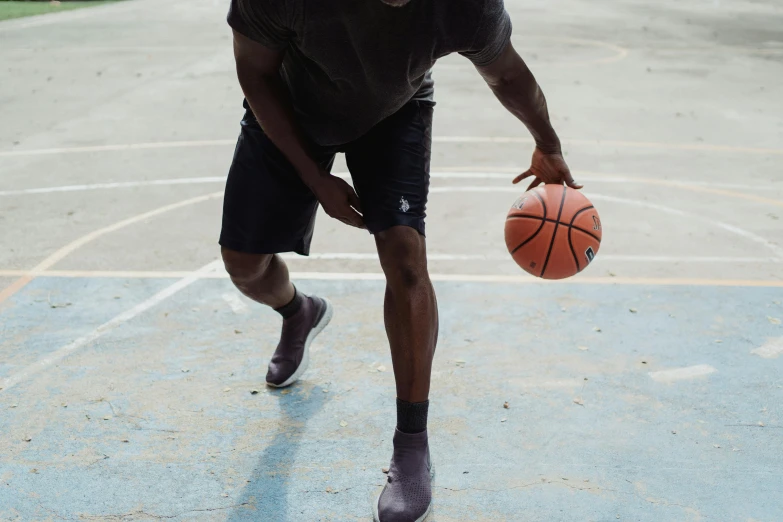 young man with hat, shirt and shorts in hand running with ball on basketball court