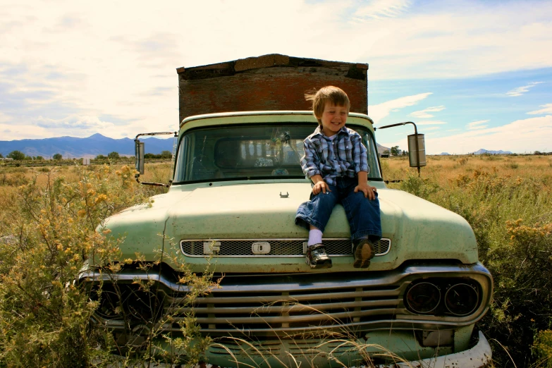 a little boy sitting on the front of an old pickup truck