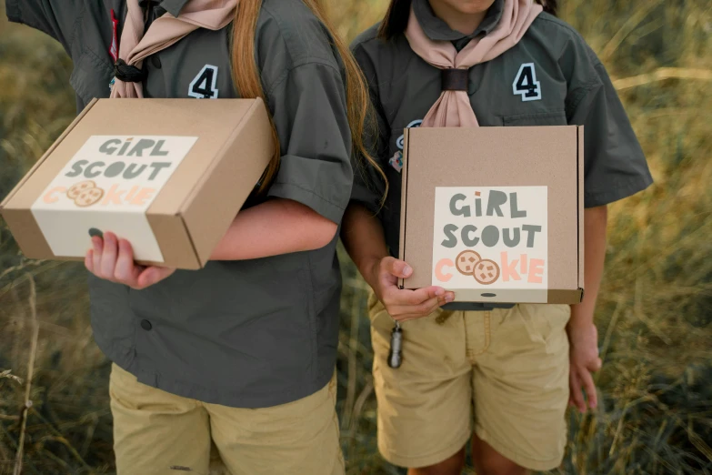 two girls hold cardboard boxes containing items for scout scouts