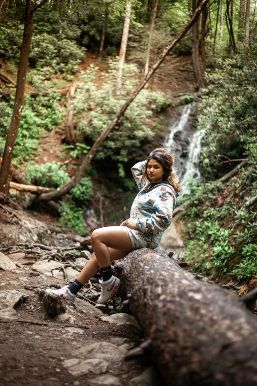 girl standing on log at edge of rocky stream in forest