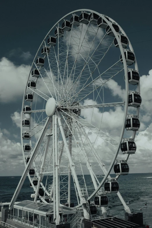 ferris wheel in front of the ocean with white clouds
