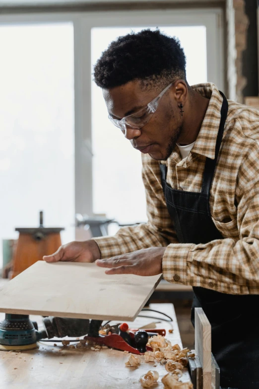 a man in glasses and workwear is working on a piece of wood