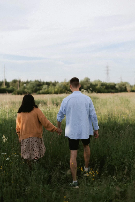 man and woman are holding hands walking through a field