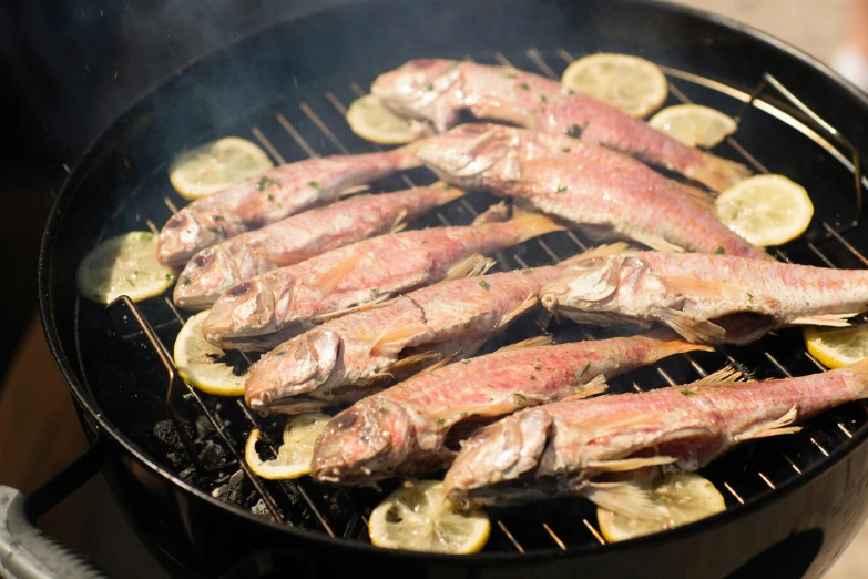 fish being cooked on a barbecue grill with lemons and charcoal