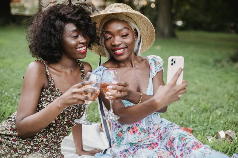 two women sitting in the grass together, using cell phones