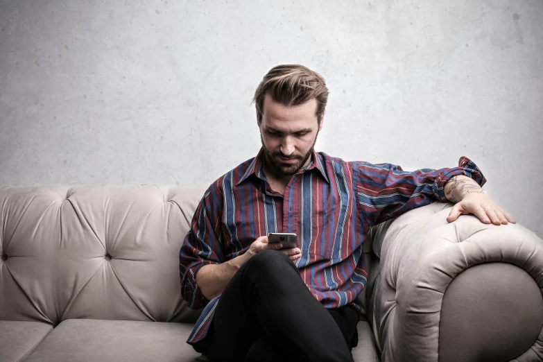 a man is sitting on a couch looking at his cell phone