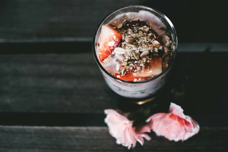 a glass of fruit topped with yogurt on top of a wooden table